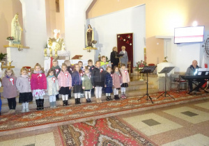 Grupa dzieci stoi pod ołtarzem w kościele.